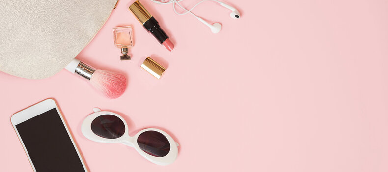 Audífonos junto a un frasco de perfume, brochas de maquillaje y un celular con un podcast en reproducción